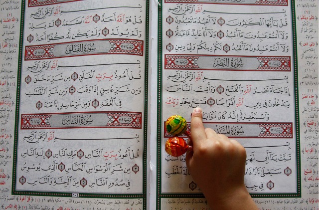 A boy holds candy in his hand as he reads the Quran in a mosque during Ramadan, in Amman, Jordan on August 22, 2009.